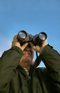 A man looking through binoculars. (focus is primarily on the lens of the binoculars).