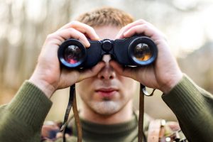 Young man looking through binoculars (army or hunting concept)